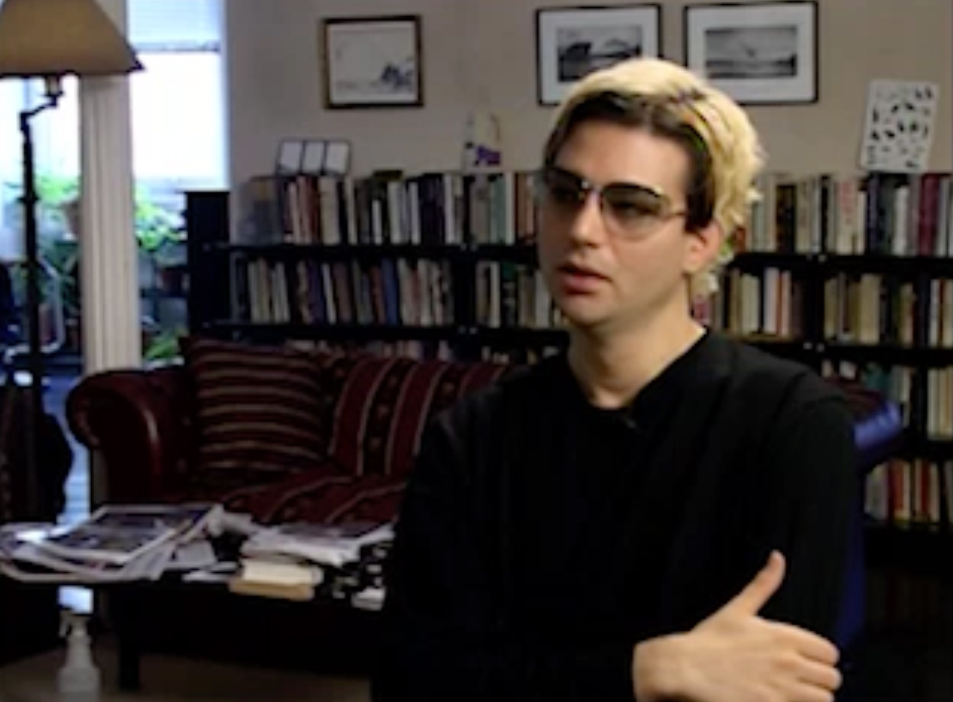 Color video. Interview set in a crowded, somewhat messy sitting room full of books on bookshelves. After close views of a black-and-white cat, the camera focuses on a man (Charles Atlas), who wears a black sweater and shaded glasses, with partially dyed yellow-blonde hair. In part b, Atlas reviews pieces of paper and smokes a cigarette. The video ends with close-ups of the cat, and shelves with small drawings, vases, and other personal curios.