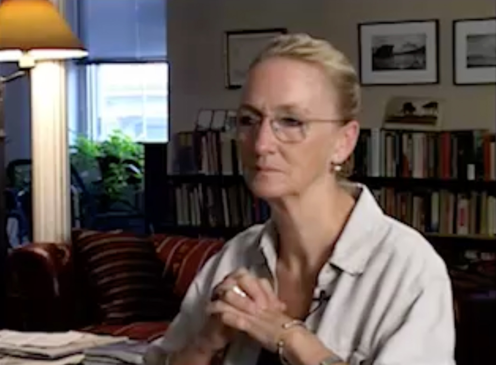 Color video of an interview set in the same living room as in other segments of Charles Atlas’s *Rainer Variations*, with camera focused entirely on a woman (Kathleen Chalfant) who wears a tight bun and blue shirt under another loose, unbuttoned collared shirt.