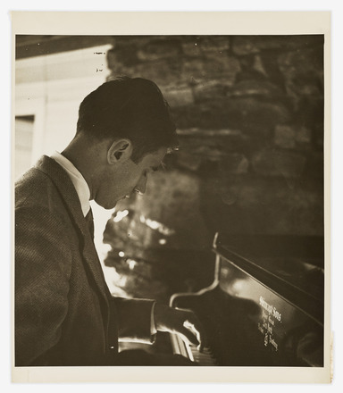 Black-and-white portrait of Tudor in a suit seated at and playing the piano. Photo taken from the right to capture the man’s profile and his left hand on the piano keys.