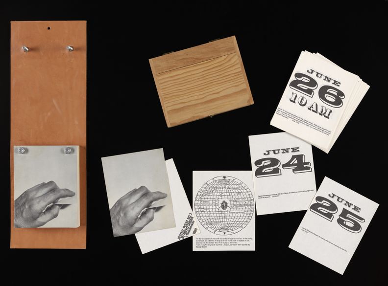 Components of a wall-mounted calendar laid out against a black background. Pages of the calendar shown include sheets with days and times, a map, and a black and white photo of a hand. Most sheets have additional, illegible text at the bottom of them.