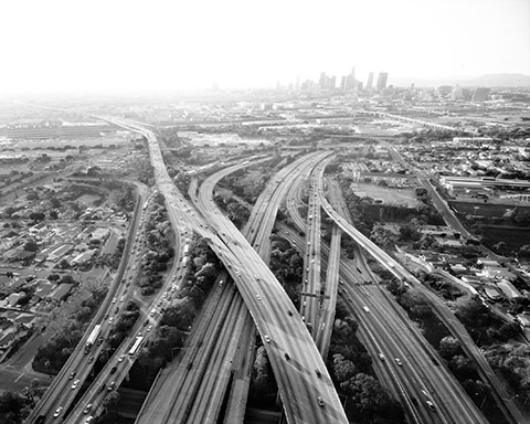 A black-and-white photograph shows an aerial view of the East Los Angeles Interchange complex, with intersections among Interstate 5, Interstate 10, State Route 60, and U.S. Route 101. 