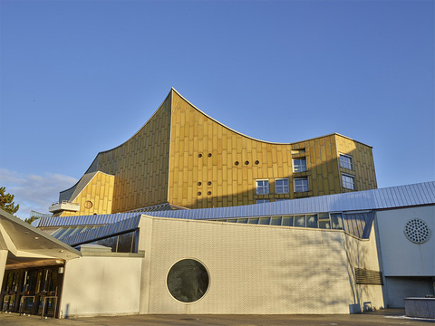 Color photo of the gold-tiled facade of the Berlin Philharmonic and one of its distinctive porthole windows in early afternoon light.