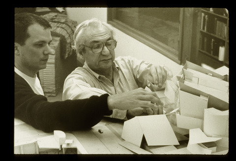 Black and white photo of Frank Gehry working with Michael Maltzan on a scale model of the Walt Disney Concert Hall.