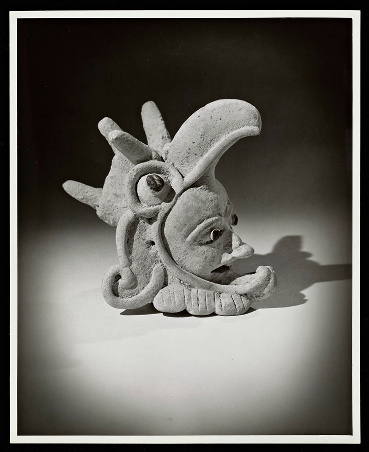 black and white photograph of a pre-columbian sculpture, a face in side a birds mouth
