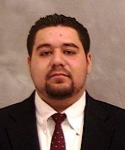 Adan Ramos wears a dark suit jacket over a white collared shirt and red tie